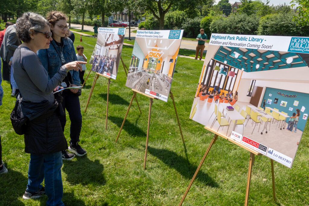 People stand in front of large easels displaying architectural renderings for the library expansion.