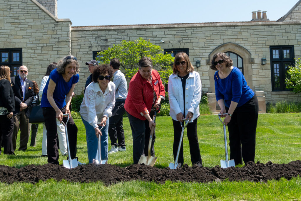 Five people stand in a line with shovels in the dirt for the groundbreaking ceremony.