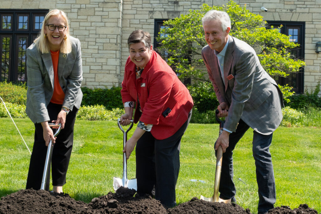 Three people stand in a row with shovels in the dirt for the groundbreaking