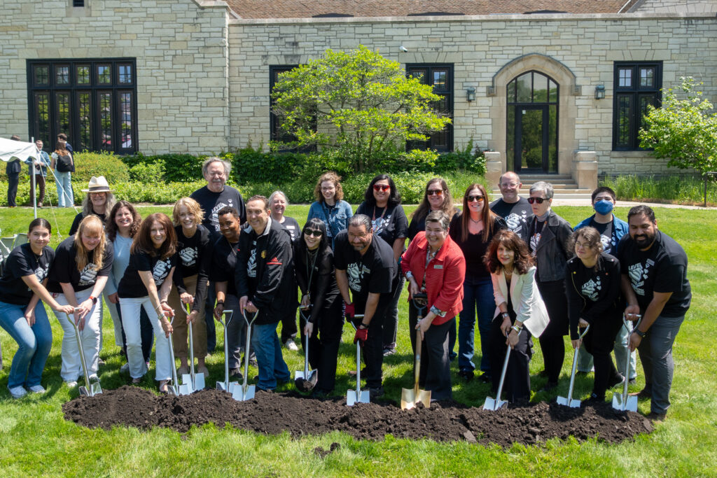 A large group of library staff pose with shovels in the dirt.