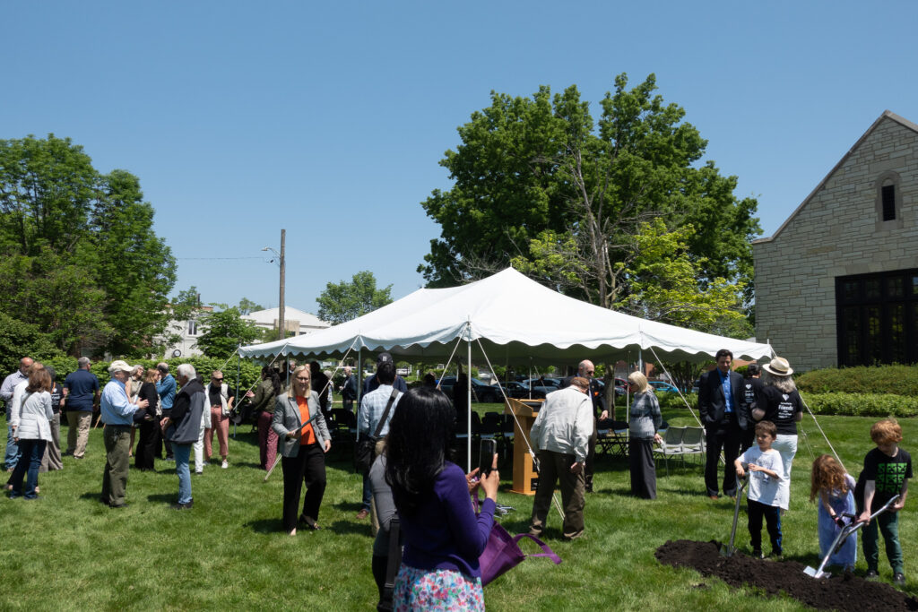 People mingle in and outside of a tent on the lawn in front of the west side of the library.