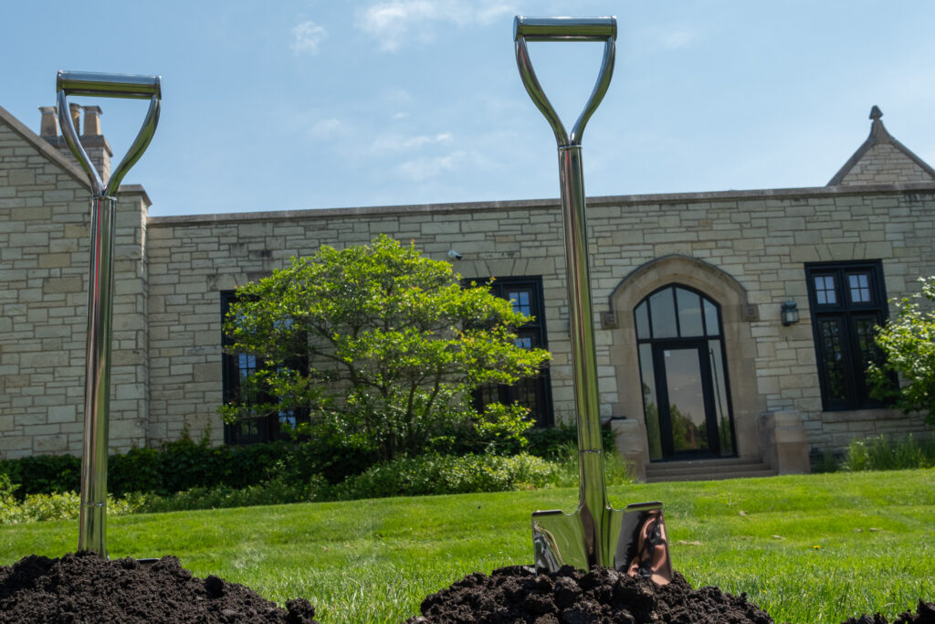 Two silver-handled shovels stand in a pile of dirt in front of the library's west side.