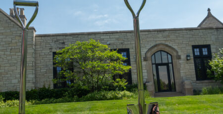 Two silver-handled shovels stand in a pile of dirt in front of the library's west side.