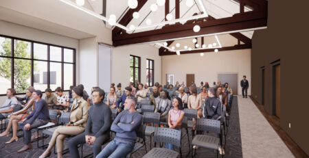 A computer generated image of a large meeting room with elaborate ceiling lighting and peaked ceiling. A group of computer-generated people are seated facing forward watching a program not in view.