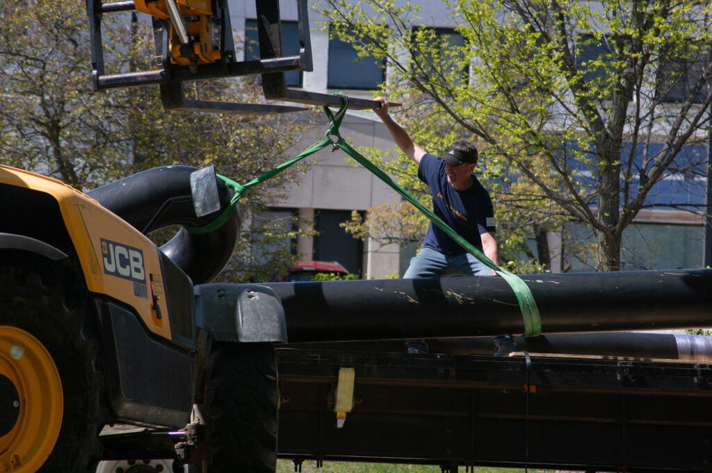 A worker guides a piece of the sculpture onto a flatbed truck. The piece is still suspended from the arm of a tractor.
