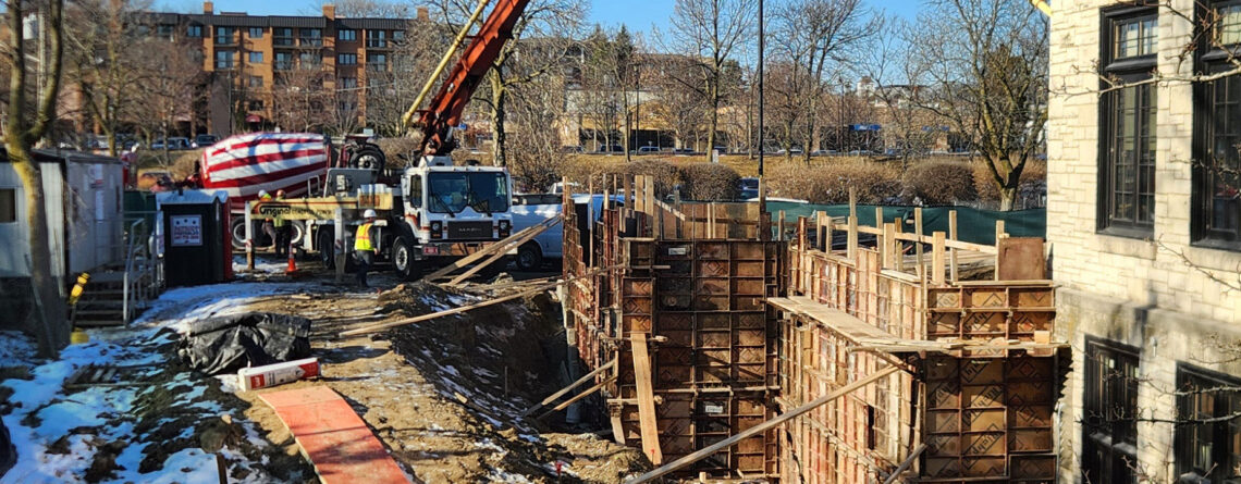 A construction crane feeds concrete into constructed footing molds.