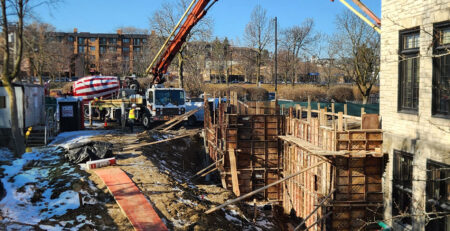 A construction crane feeds concrete into constructed footing molds.