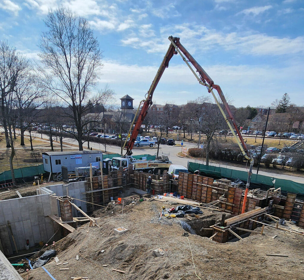 Concrete for footings is poured via crane. The forms for set footings are removed.
