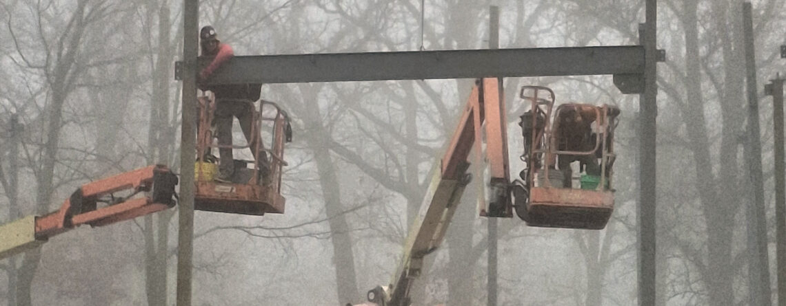 A worker in a lift attaches a steel beam to a steel post.