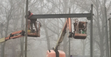 A worker in a lift attaches a steel beam to a steel post.