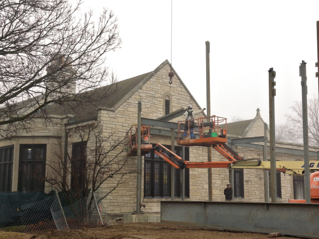 Worker in a lift attaches steel beams to the existing library structure.