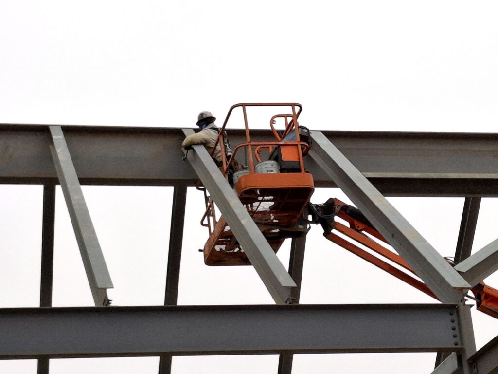 A worker uses a lift to attach a steel roof beam.