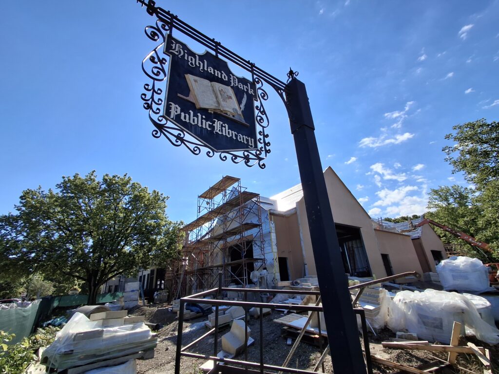 Photo of current exterior expansion construction. A vintage Highland Park Public Library sign hangs in the foreground.