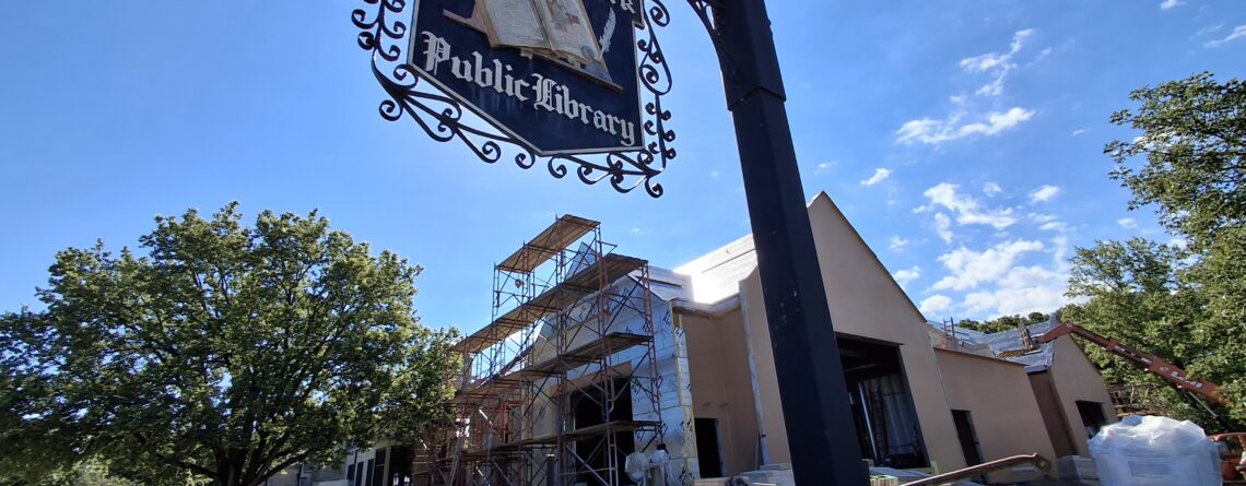 Photo of current exterior expansion construction. A vintage Highland Park Public Library sign hangs in the foreground.