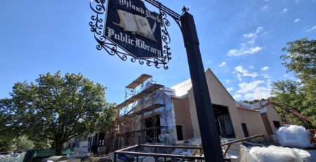 Photo of current exterior expansion construction. A vintage Highland Park Public Library sign hangs in the foreground.